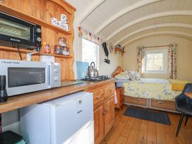 A small living space with a kitchen area including microwave and fridge and a bed with floral bedding at Roach Hut in Hadlow Down near Crowborough