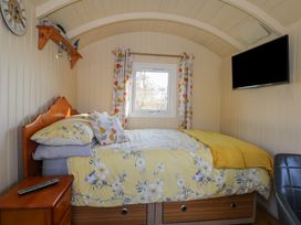 A bedroom with a bed yellow floral bedding a window with patterned curtains a wall clock and a wall mounted television at Roach Hut in Hadlow Down near Crowborough