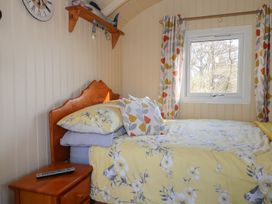 A bedroom with a wooden bed with yellow floral bedding a wooden nightstand with a remote and a window with patterned curtains at Roach Hut in Hadlow Down near Crowborough
