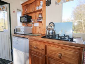 A kitchen counter with a stove kettle microwave fridge and wooden shelves with glasses at Roach Hut in Hadlow Down near Crowborough