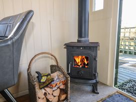 A wood burning stove with fire inside next to a basket of firewood in a room at Roach Hut in Hadlow Down near Crowborough