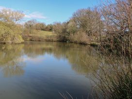 A pond surrounded by trees and bushes under a blue sky at Roach Hut in Hadlow Down near Crowborough
