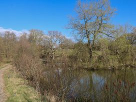 A pond with trees and bushes around it and a gravel path under a blue sky at Roach Hut in Hadlow Down near Crowborough