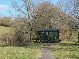 A small green cabin on stilts in a grassy area with leafless trees and a gravel path leading to it at Roach Hut in Hadlow Down near Crowborough
