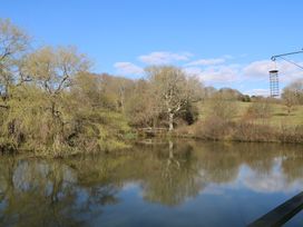 A view of a pond with trees and a small wooden bridge in the background at Roach Hut in Hadlow Down near Crowborough