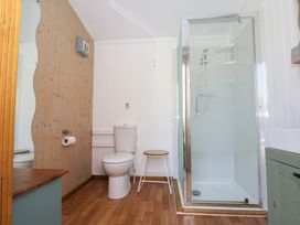 A bathroom with a toilet a stool a glass shower enclosure wooden flooring and a wooden panel wall at Roach Hut in Hadlow Down near Crowborough