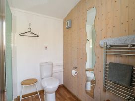 A bathroom with a toilet a small wooden stool a wall-mounted wavy mirror and a towel rack with towels at Roach Hut in Hadlow Down near Crowborough