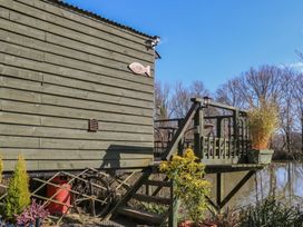 An exterior view of a wooden hut with a deck overlooking a pond and surrounded by plants at Carp Hut in Hadlow Down near Crowborough