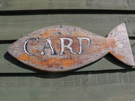A wooden fish-shaped sign with the word carp mounted on a green wooden wall at Carp Hut in Hadlow Down near Crowborough