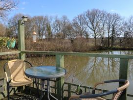 A deck with two wicker chairs a round glass table and a bird feeder overlooking a pond with trees in the background at Carp Hut in Hadlow Down near Crowborough