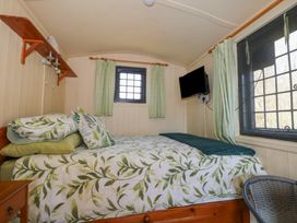 A bedroom with a double bed with leaf patterned bedding a wall mounted television and two windows at Carp Hut in Hadlow Down near Crowborough