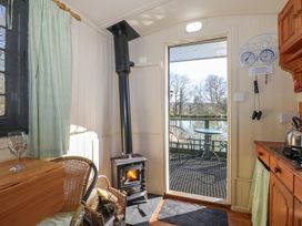 A small room with a wood stove a chair and a table outside by a lake at Carp Hut in Hadlow Down near Crowborough
