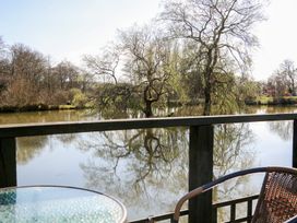 A glass table and a wicker chair on a balcony overlooking a lake with trees reflected in the water at Carp Hut in Hadlow Down near Crowborough