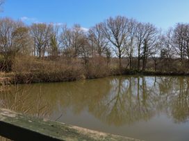 A pond surrounded by leafless trees and bushes under a blue sky at Carp Hut in Hadlow Down near Crowborough