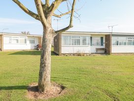 A tree in front of two single-storey houses with grass lawns at Chalet 21 in Newport Norfolk