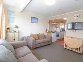 A living room with two sofas a wall mounted TV and an open kitchen area at Chalet 21 in Newport Norfolk
