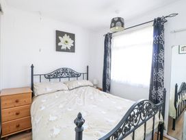 A bedroom with a metal bed frame a wooden dresser a window with curtains and a floral painting above the bed at Chalet 21 in Newport Norfolk
