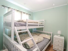A bedroom with a white bunk bed a nightstand with a lamp and curtains on the window at Chalet 21 Newport Norfolk