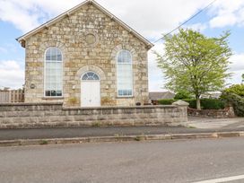 The exterior of a stone building with arched windows and a white door behind a stone wall and a tree at Trelowth Chapel in Polgooth