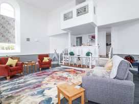 A living room with two red armchairs a gray sofa a wooden side table a colorful rug and white decorative balcony at Trelowth Chapel in Polgooth