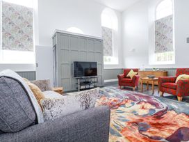 A sitting room with a gray sofa red armchairs a colorful rug and a television at Trelowth Chapel in Polgooth
