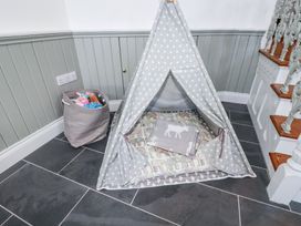 A corner with a small gray teepee tent on a tiled floor with a basket of toys and stairs nearby at Trelowth Chapel in Polgooth