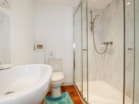 A bathroom with a white sink, toilet, glass-enclosed shower with a handheld showerhead and a blue bath mat on the floor at Trelowth Chapel in Polgooth