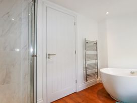 A bathroom with a white door a chrome towel radiator a white bathtub and a tiled shower area at Trelowth Chapel in Polgooth