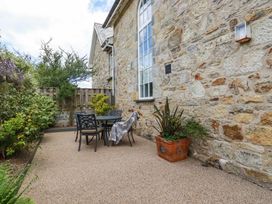 An outdoor patio area with a table and four chairs next to a stone wall with a window and plants around at Trelowth Chapel in Polgooth