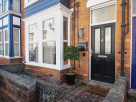 The entrance to a brick house with a black door a welcome mat a potted plant and a white bay window