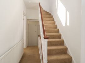 A carpeted staircase with white banisters and wooden handrail in a hallway with white walls and doors at Seaside House in Weymouth