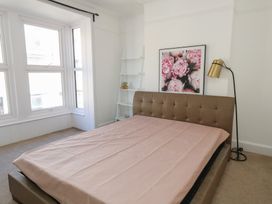 A bedroom with a large bed covered with a beige sheet a white ladder shelf with a teddy bear a gold floor lamp and a floral picture on the wall at Seaside House in Weymouth