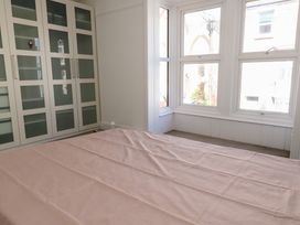 A bedroom with a bed covered by a pink sheet near a large window and a white wardrobe with frosted glass doors at Seaside House in Weymouth