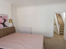 A bedroom with a bed covered with a pink sheet a framed floral picture on the wall and a staircase visible through an open door at Seaside House in Weymouth