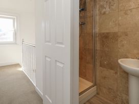 A hallway with a white railing and window next to a bathroom with a shower and a sink at Seaside House in Weymouth