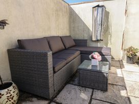 An outdoor patio area with a rattan sofa and coffee table with flowers and potted plants against a corner wall