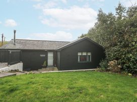 A black wooden house with a tiled roof and a green lawn in front with bushes on one side at Chy Benyngoth in Hayle
