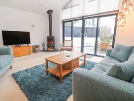 A living room with a blue rug wooden coffee table two sofas a television wood stove and glass doors leading outside at Chy Benyngoth in Hayle