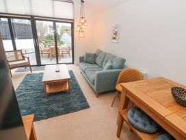 A living room with a teal sofa wooden coffee table and outdoor seating visible through sliding glass doors at Chy Benyngoth in Hayle