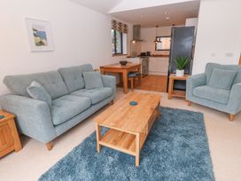 A living room with two blue sofas a wooden coffee table and a blue rug near a kitchen at Chy Benyngoth in Hayle