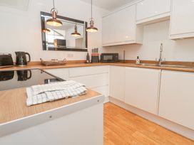 A kitchen with white cabinets wooden countertops a stovetop a sink a microwave and a black kettle at Chy Benyngoth in Hayle