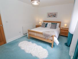 A bedroom with a wooden double bed with pillows and a throw a white rug on a blue carpet two wooden bedside tables with lamps and a painting on the wall at Chy Benyngoth in Hayle