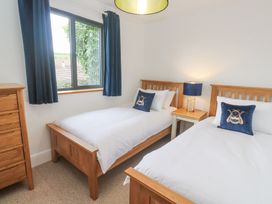A bedroom with two single beds with wooden frames a wooden chest of drawers a bedside table with a lamp and a window with blue curtains at Chy Benyngoth in Hayle