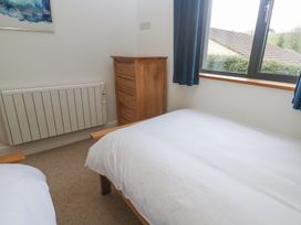 A bedroom with a bed white bedding wooden dresser blue curtains and a window at Chy Benyngoth in Hayle