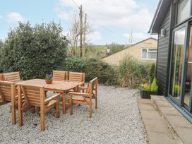An outdoor seating area with a wooden table and six chairs on gravel beside a black building at Chy Benyngoth in Hayle