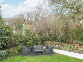 An outdoor seating area with chairs a loveseat and a table surrounded by greenery and trees at Chy Benyngoth in Hayle