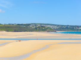 A beach with sand and water channels with houses on hills in the background at Chy Benyngoth in Hayle