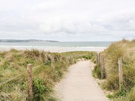 A wooden boardwalk path through grassy sand dunes leading to a beach with the ocean and clouds in the background at Chy Benyngoth in Hayle
