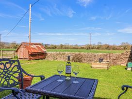 A garden with a black table and two chairs with a bottle of wine and two glasses on the table at The Yarde Annexe in Pen Elm near Taunton