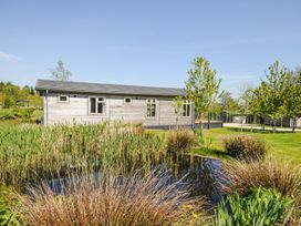 A wooden cabin by a pond with reeds and trees on a grassy lawn at 17 Meadow Retreat in Dobwalls